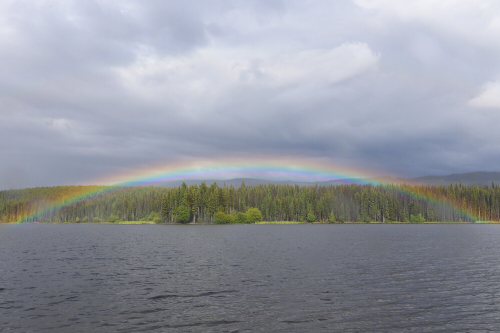 A complete rainbow arc encompasses a lake and it's shoreline stretching into the clouds.